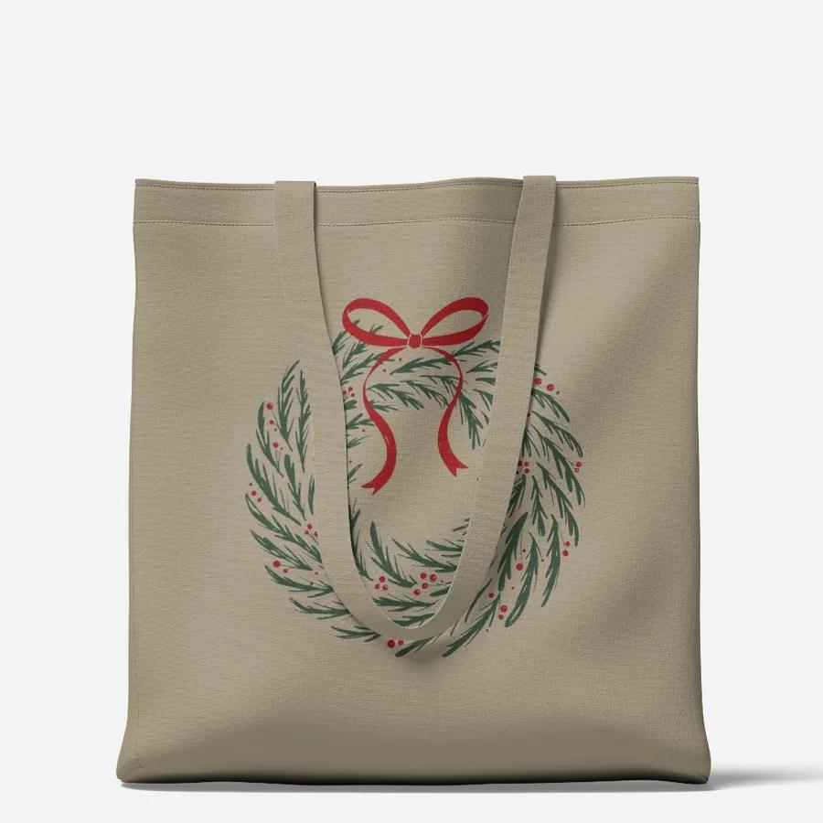 A sand tote bag printed with the pine and holly wreath